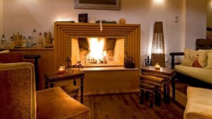 A cozy living room with a fireplace, wooden furniture, and wall-mounted sconces. - Maistros Exclusive Suites (Rethymno)