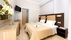 A hotel room with a bed, bedside tables, a TV mounted on the wall, and a vase with flowers on a wooden dresser. - Amalia Corfu Hotel - Adults Only (Corfu)