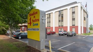 Een bord met 'Studios & 4 Suites', met mogelijkheden voor een dag- of langdurig verblijf, voor een gebouw met een parkeerplaats.