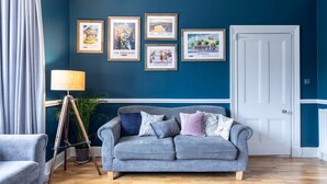 A living room with a grey sofa, a lamp, and framed pictures on the wall. - West of the Ness • Large City Home • Hot Tub (Inverness)
