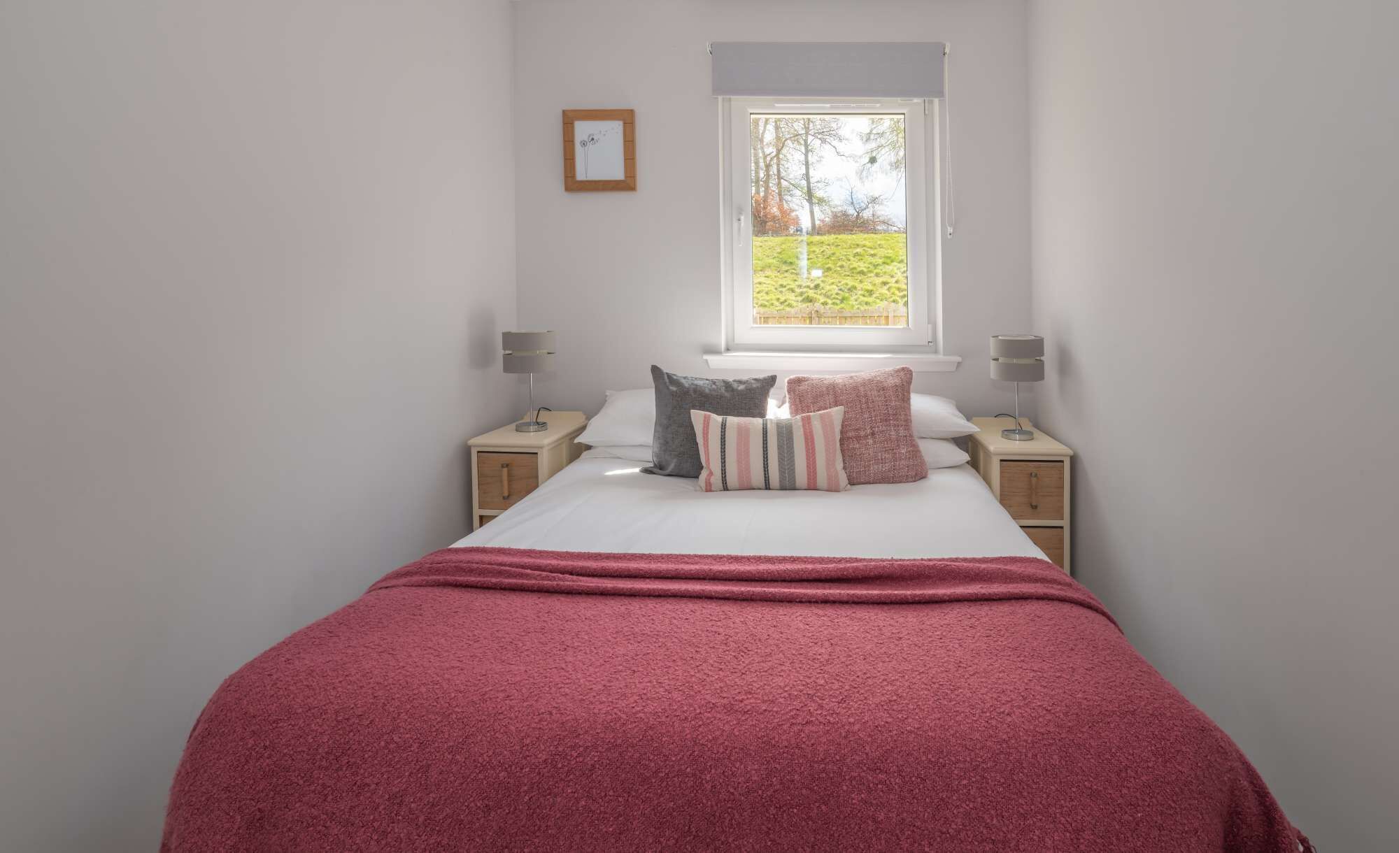 A bedroom with a bed, two bedside tables, a window, and a picture on the wall.