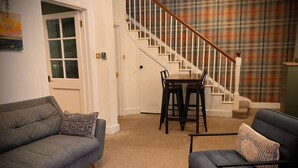 Un salon avec un canapé gris, un fauteuil bleu, un tapis à motifs et un mur décoré d’un motif à carreaux.