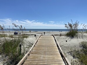 Walk along the boardwalk to the sandy beach, surrounded by lush greenery.
