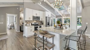 A modern kitchen with white cabinets, stainless steel appliances, and a large island with bar stools. - Single level Sea Pines home with a hot tub, just a short walk to the beach! (Hilton Head)