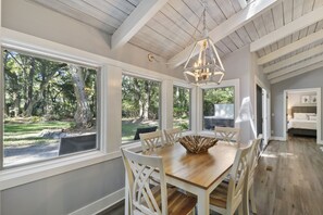 Relax in a spacious dining area with a large table and comfortable seating, surrounded by natural views and a high ceiling.
