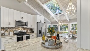A modern kitchen with white cabinets, stainless steel appliances, and a large island with a tray of wine bottles. - Single level Sea Pines home with a hot tub, just a short walk to the beach! (Hilton Head)