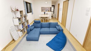 Ein kompakter Wohnbereich mit einem blauen Modulsofa, einem kleinen Esstisch und einer Küchenzeile im Hintergrund.