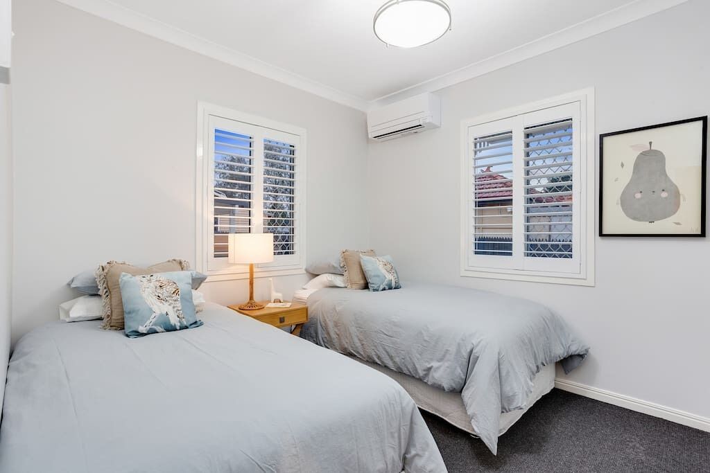 A bedroom with two beds, a nightstand, and a window with blinds.