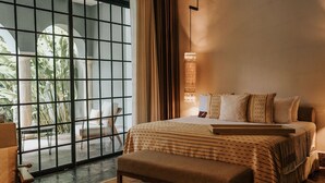 A modern bedroom with a large bed, a bench, and a view through a glass door to an outdoor area. - Antelar Casa Destino (Mérida)
