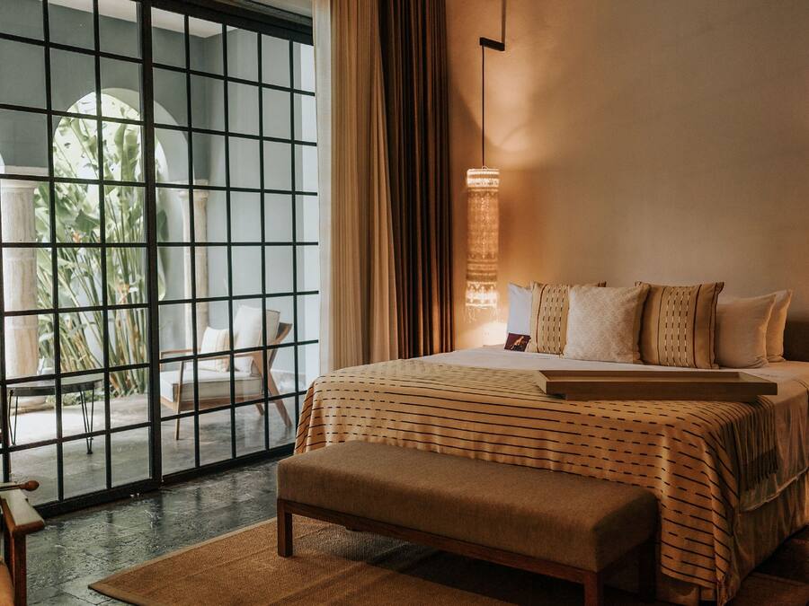 A modern bedroom with a large bed, a bench, and a view through a glass door to an outdoor area.