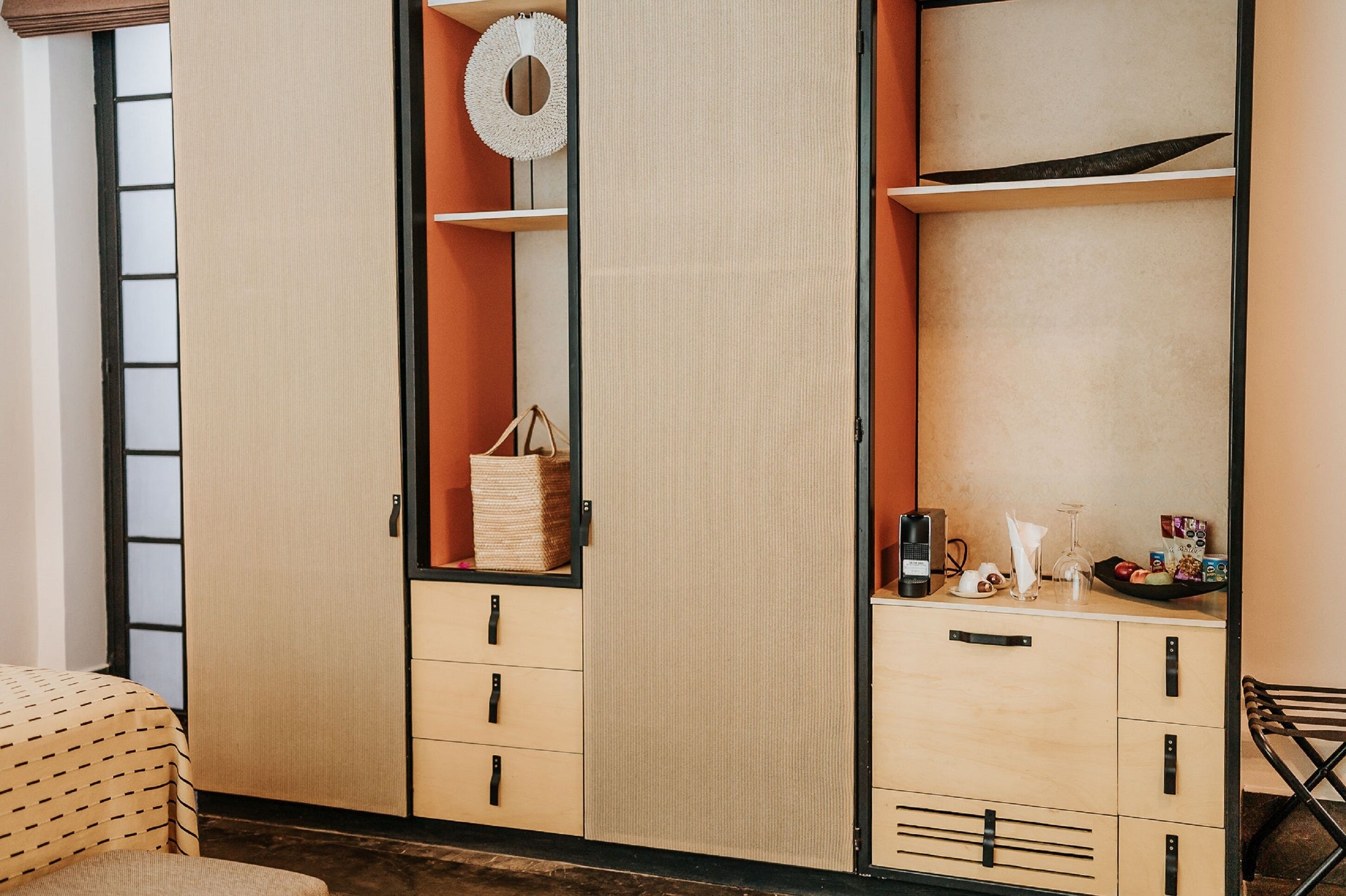 A room with a bed, a wardrobe with multiple compartments, a small table with a lamp, and a chair.