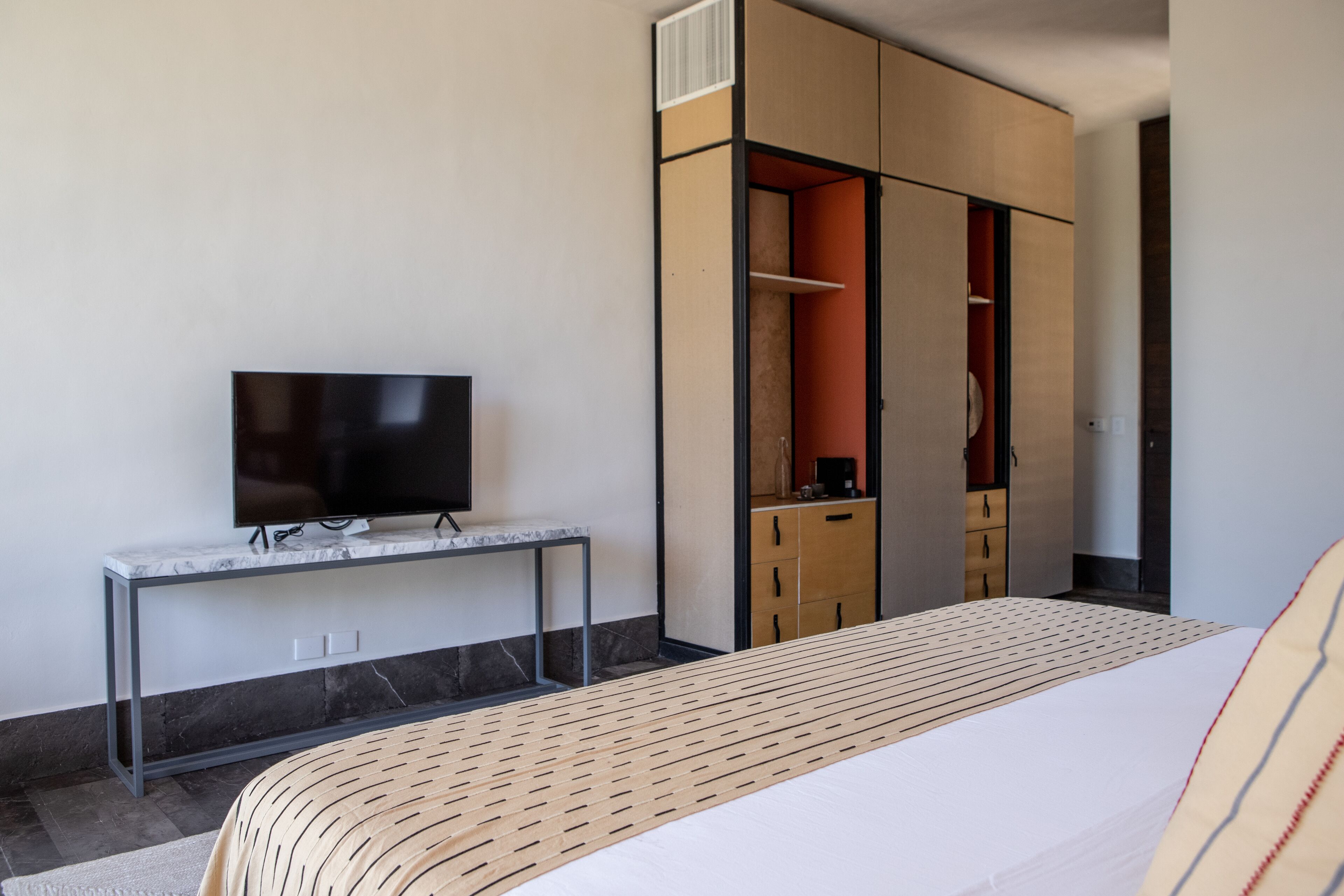 Quarto de hotel moderno com cama, TV sobre console de mármore e guarda-roupa com portas de correr.