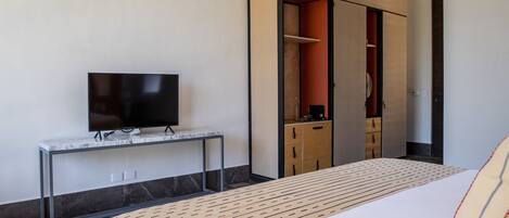 Quarto de hotel moderno com cama, TV sobre console de mármore e guarda-roupa com portas de correr.