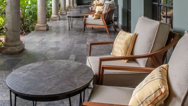 A covered outdoor seating area with stone columns, wicker furniture, and a round table. - Antelar Casa Destino (Mérida)