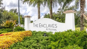 A sign for "The Enclaves at Festival" with a landscaped garden in the foreground. - Amazing New 5 Bedroom 4.5 Bathroom Townhome with Private Pool (Davenport)