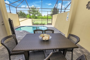 Ein überdachter Patio mit Pool, Korbmöbeln und einem Tisch mit Dekoration.