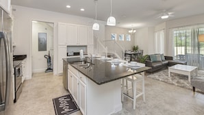 A modern kitchen with a central island, white cabinetry, and a dining area with a table and chairs. - Amazing New 5 Bedroom 4.5 Bathroom Townhome with Private Pool (Davenport)