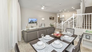 A modern living room with a dining area, a staircase, and a kitchen in the background. - Amazing New 5 Bedroom 4.5 Bathroom Townhome with Private Pool (Davenport)