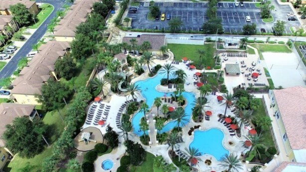 An aerial view of a resort with multiple swimming pools, palm trees, and a parking lot. - Amazing Townhouse 4Bdr 3Bth Spa Resort near Disney (Davenport)