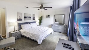 A hotel room with a bed, bedside tables, a desk with a TV, a ceiling fan, and artwork on the walls. - Amazing Townhouse 4Bdr 3Bth Spa Resort near Disney (Davenport)