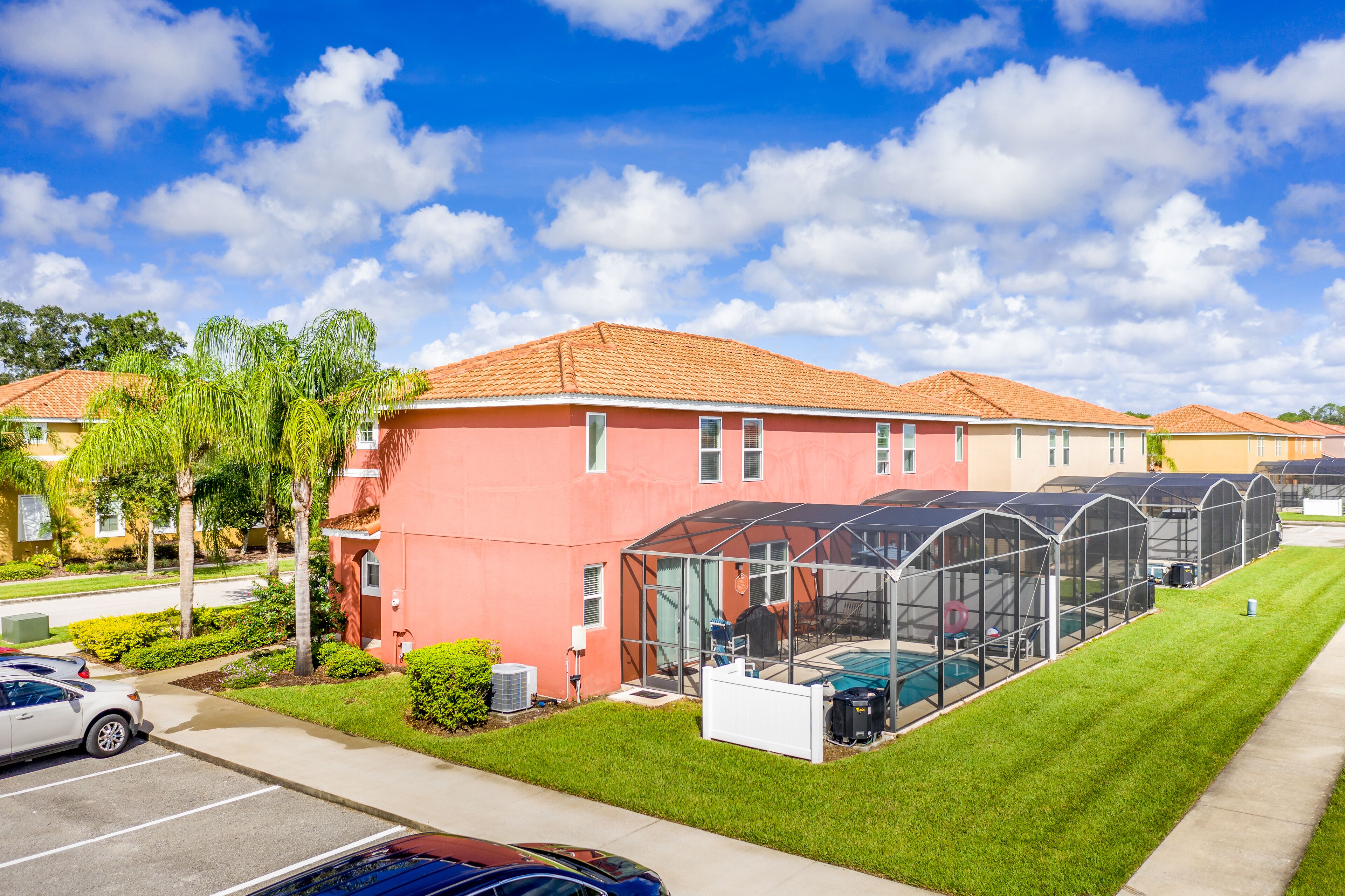 A multi-story building with a red facade, a covered outdoor swimming pool, and a parking lot with several cars.