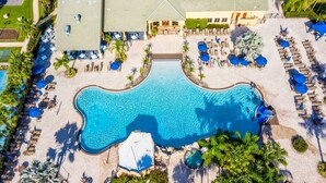 An aerial view of a resort with a large swimming pool, sun loungers, and palm trees.