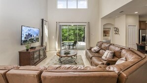 A spacious living room with a large brown leather sofa, a coffee table, and a television on the wall.