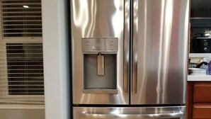 A stainless steel refrigerator with a water dispenser, wooden cabinets, and a window with blinds. - A Luxury Urban Getaway Walk to Stanford #2333 (Palo Alto)