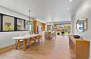 A modern kitchen with wooden cabinets, a dining area with a round table, and a view of a waterfall and pool outside.