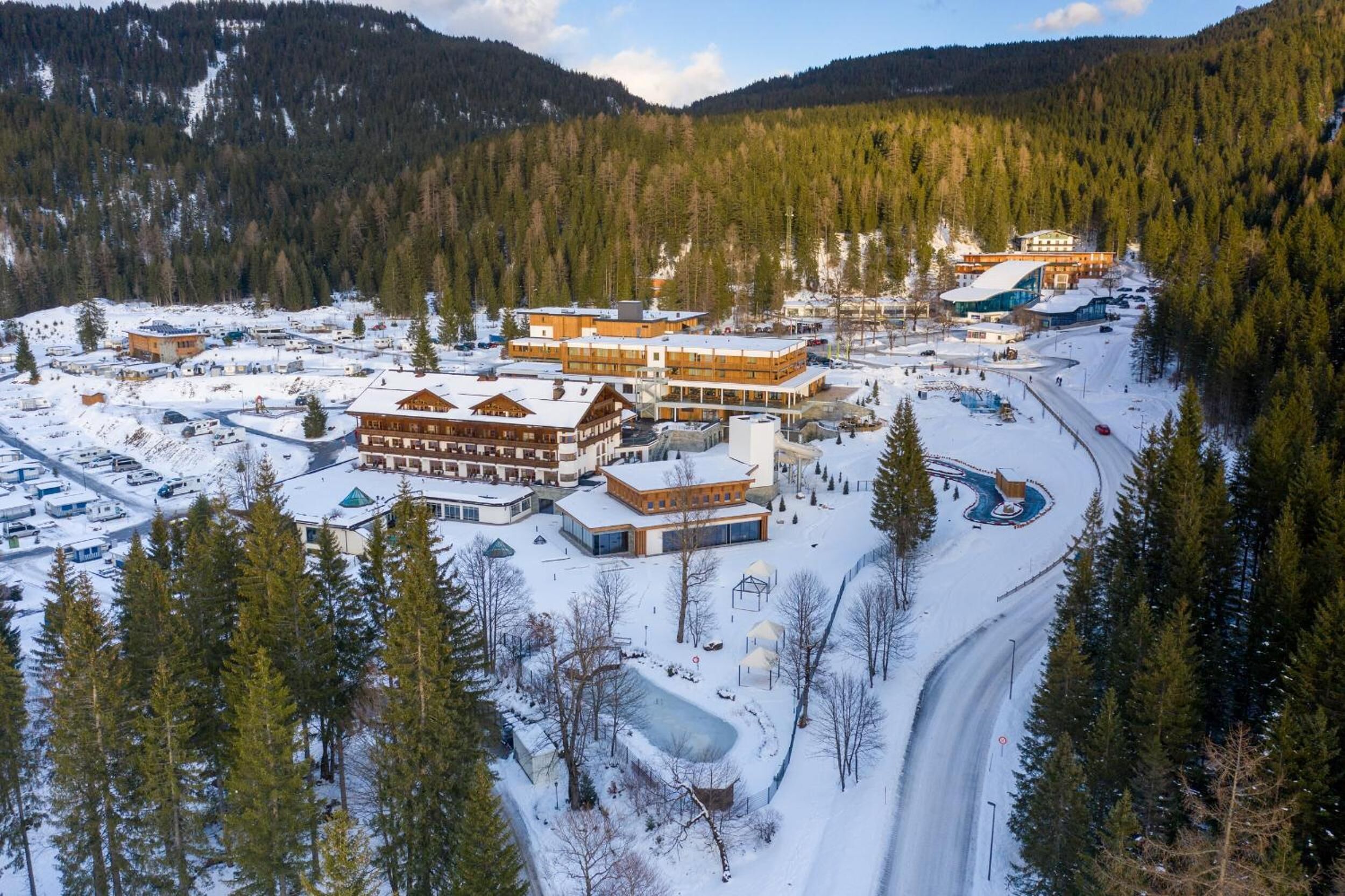 A snow-covered resort with multiple buildings, including a large lodge and smaller cabins, surrounded by dense forests and a ski slope.