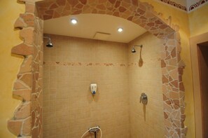 Zona de ducha con diseño de arco de piedra, paredes con azulejos e iluminación en el techo.