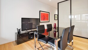 A modern living room with a flat-screen TV, a glass coffee table, and black leather chairs.