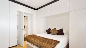 A modern bedroom with a large bed, white walls, and a wooden floor.