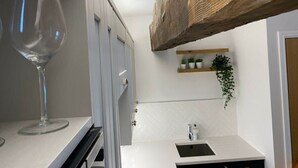 Una cucina con mobili bianchi, una trave in legno, un bicchiere da vino e una piccola pianta su uno scaffale.