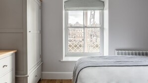 Una camera da letto con un'ampia finestra, un letto, una cassettiera e un termosifone.