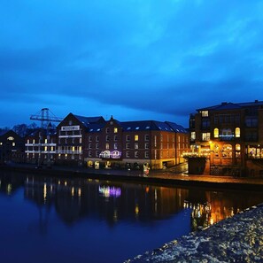 Ett hotell vid vattnet med flera byggnader, inklusive en framträdande skylt med texten ”Woodsmill”, och en stilla flod som speglar byggnaderna.