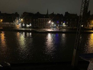 A nighttime view of a riverside area with buildings reflecting on the water, a bridge, and a crane structure. - Woodsmill View - 5 Star - River view- Balcony (York)