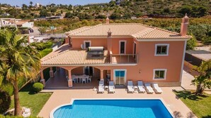 Una casa de dos pisos con piscina, un patio cubierto y vistas de las colinas circundantes.