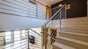 Una escalera moderna con barandillas de metal, peldaños color beige y una pared oscura con obras de arte.