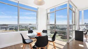 Een moderne eetruimte met een glazen tafel, zwarte stoelen en een stadszicht door grote ramen.
