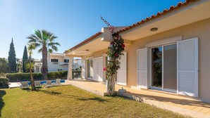Una villa moderna con un prato curato, persiane bianche e cielo azzurro limpido.