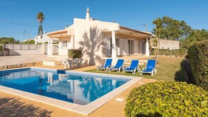 Un'area piscina con piscina, sedie a sdraio e un edificio con tetto in tegole.