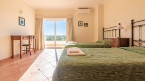 Hotelkamer met twee bedden, een bureau en een stoel. Er is een balkon met gordijnen en uitzicht op de stad.