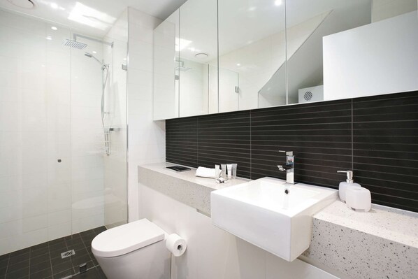 A modern bathroom with a glass shower enclosure, a white toilet, and a sink with a black-tiled backsplash. - Split-Level Executive 2BR Darlinghurst Apartment with a New York Feel (Darlinghurst)