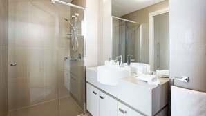 Un baño moderno con ducha envuelta en vidrio, un lavamanos blanco y un espejo grande.