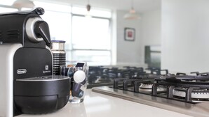 A Nespresso coffee machine on a kitchen counter with a glass of water and a cup of coffee. - Modern and Bright 3BR Executive Apartment in Zetland with Views (Zetland)