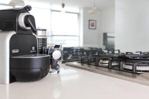 Nespresso-kahvinkeitin keittiön työtasolla, sen vieressä lasi vettä ja kahvikuppi.
