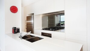 A modern kitchen with white cabinetry, stainless steel appliances, a sink, and a red clock on the wall. - Modern and Bright 3BR Executive Apartment in Zetland with Views (Zetland)