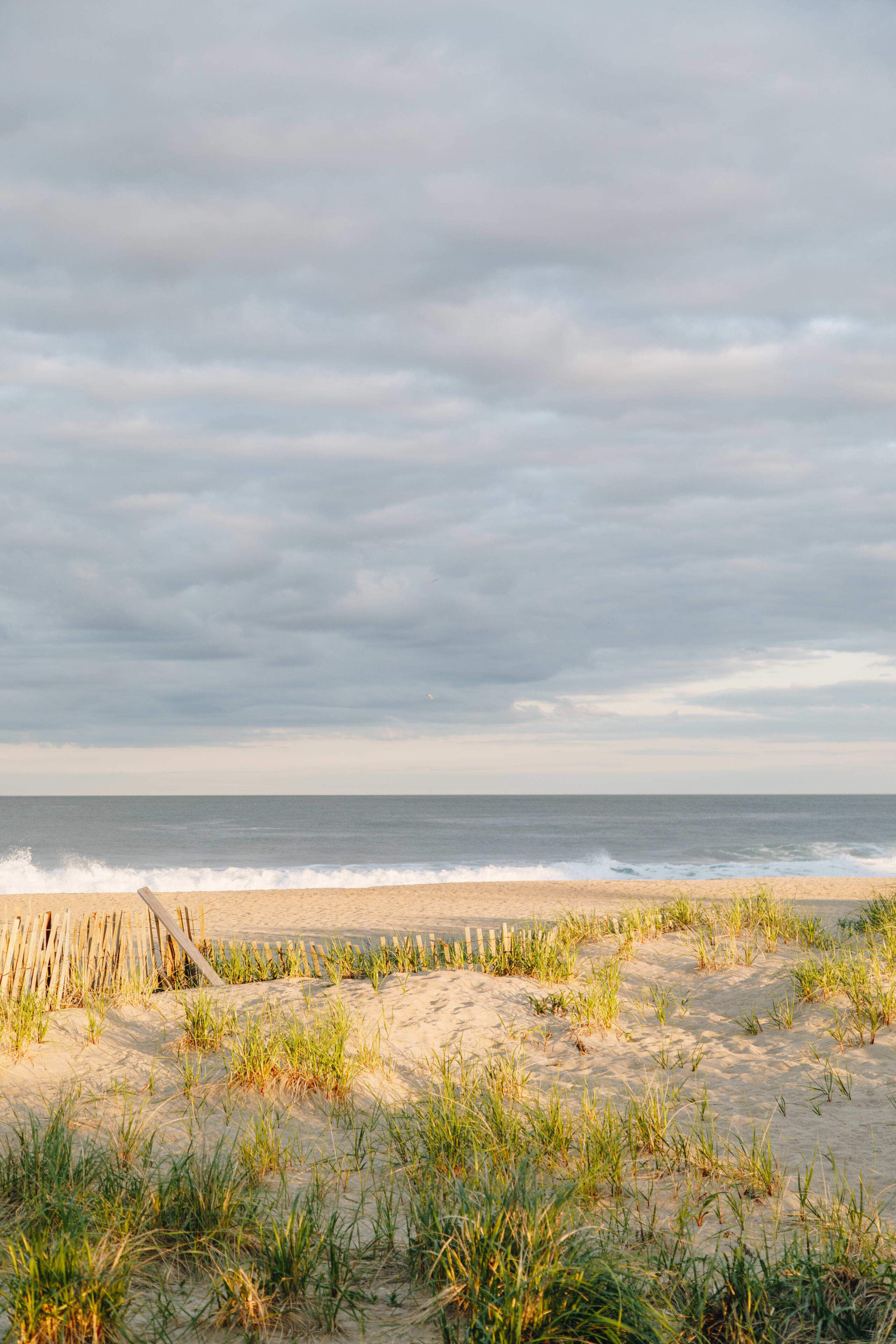 A beach with a wooden fence and sand dunes.