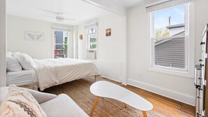 Une chambre à coucher avec un lit, un banc blanc, un ventilateur de plafond et une fenêtre avec des stores.